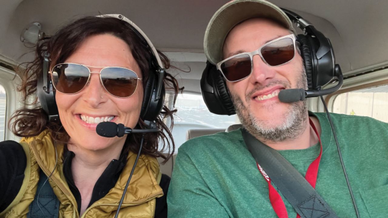 On the left is writer Maggie Ginsberg and on the right is pilot Shane Baker, both wearing sunglasses and headsets in the cockpit of an airplane.