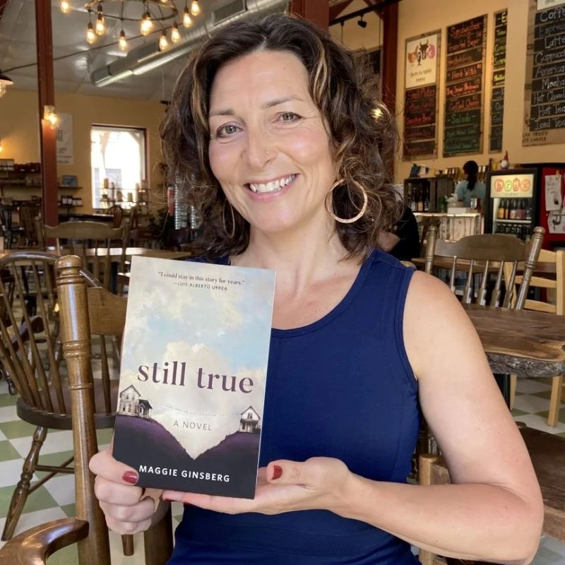 Maggie Ginsberg holds her novel, 'Still True" up in a coffee shop. 