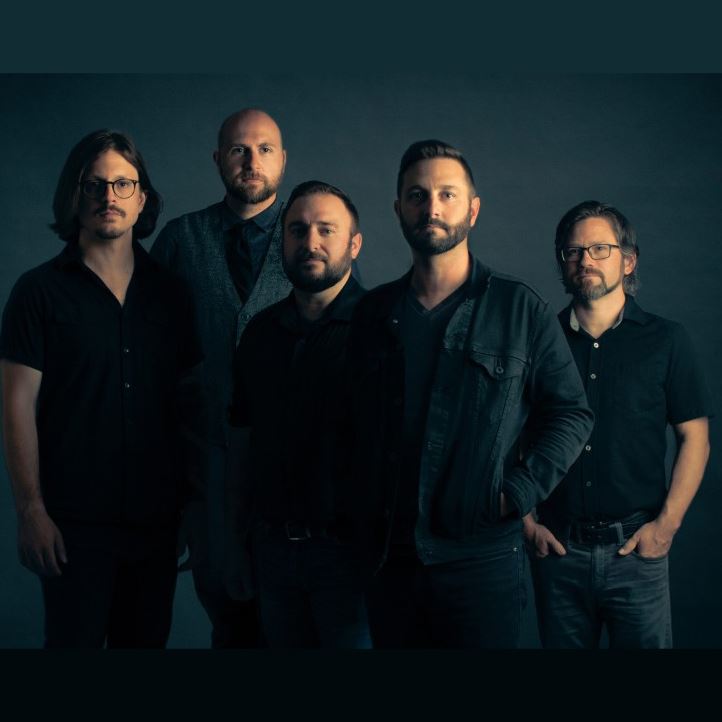 a dark and moody group portrait five men, all with beards except one, one guy has just a mustache