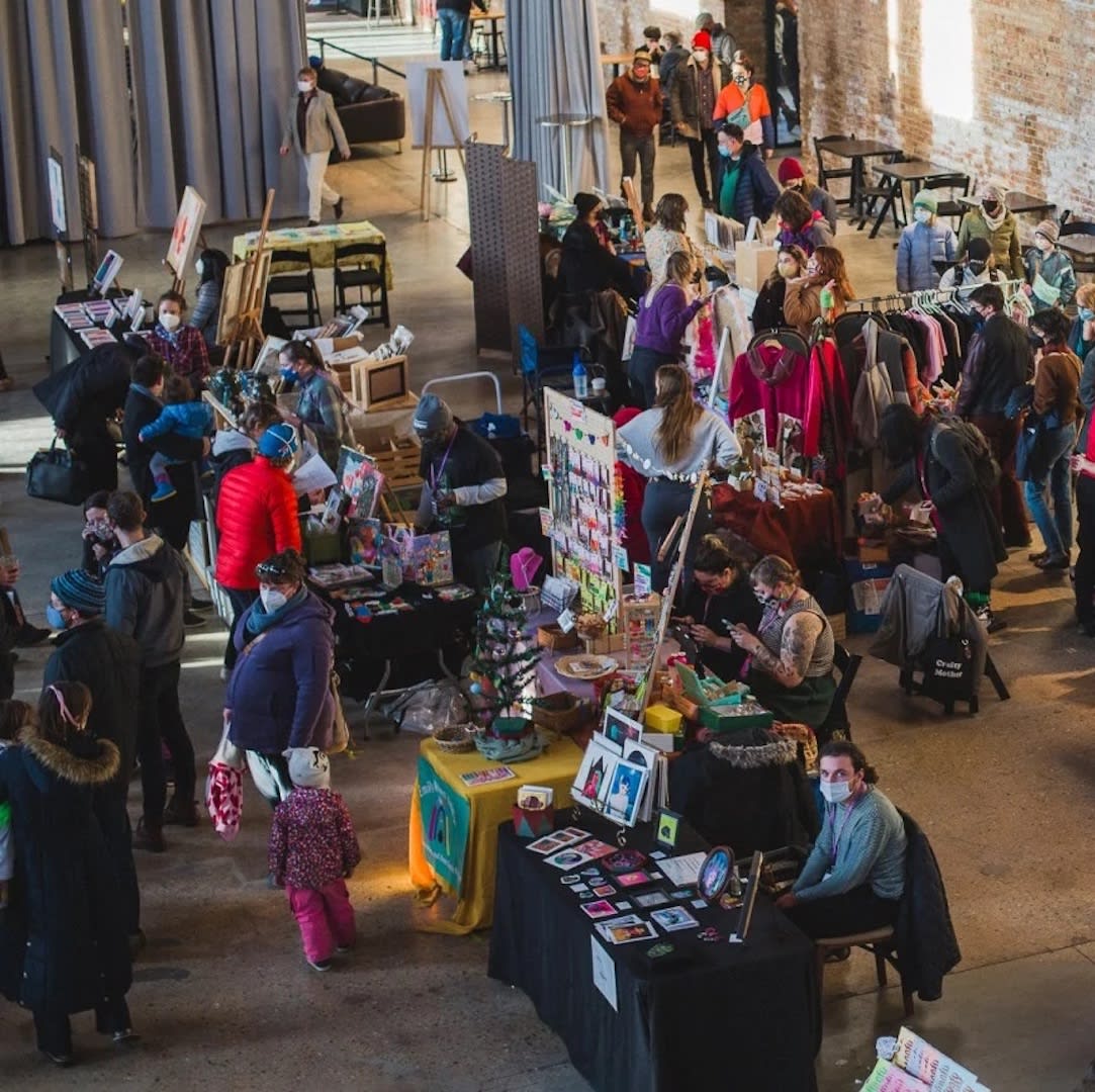 Overhead shot of a market filled with artisans selling their work at craft stands and visitors milling through.