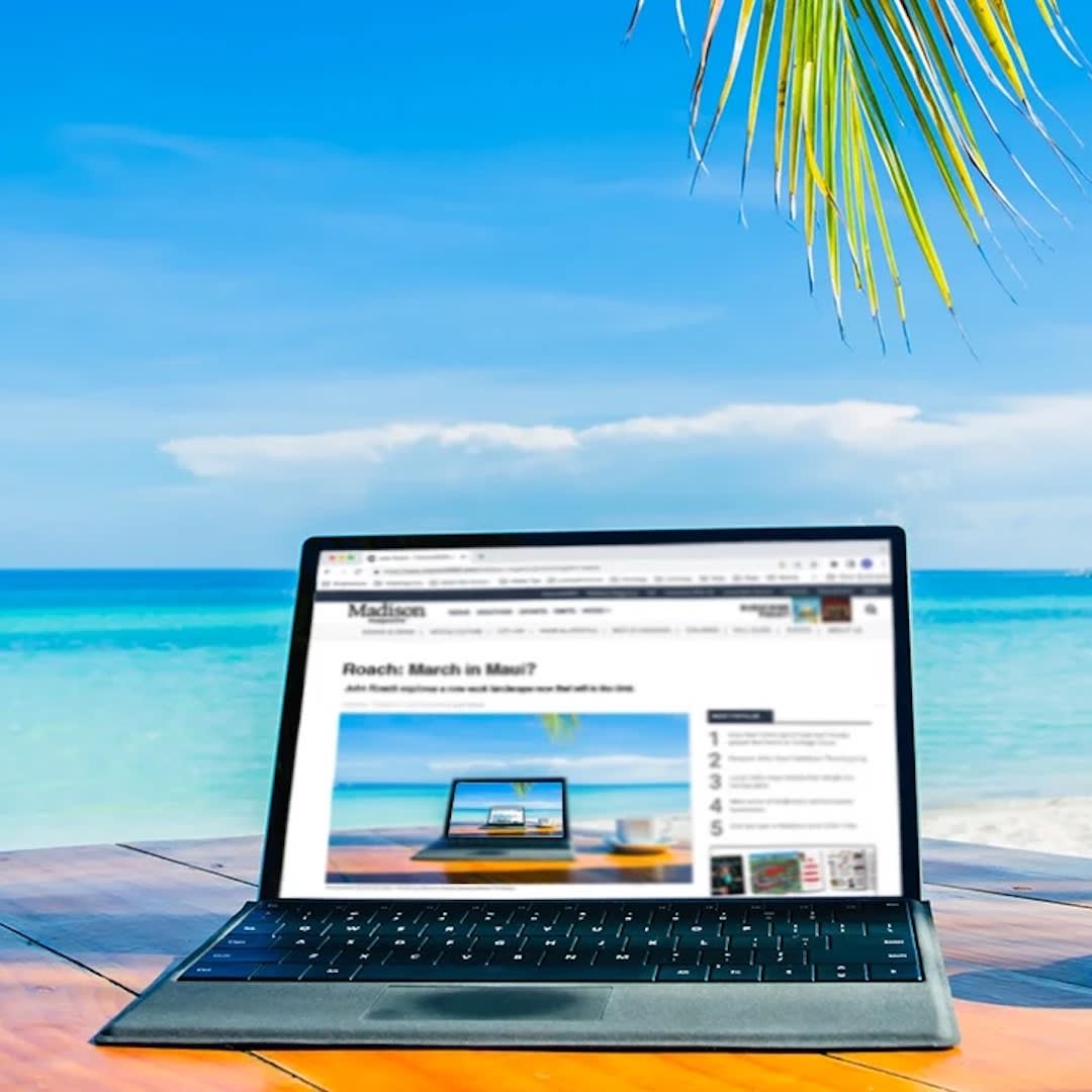 Image of a computer sitting on a wooden table with a blue ocean in the background.