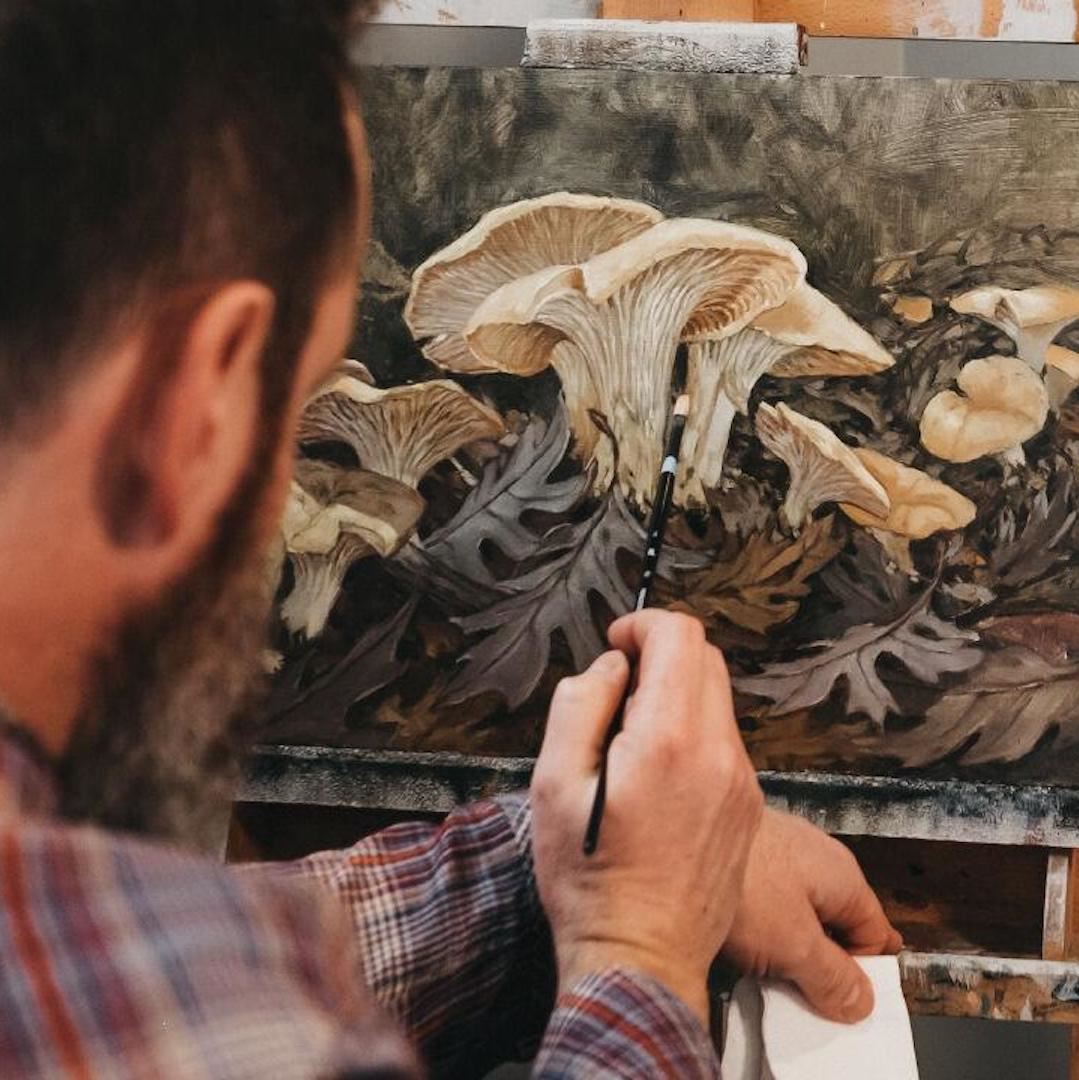 View over Mangerson's shoulder of him painting realistic mushrooms.