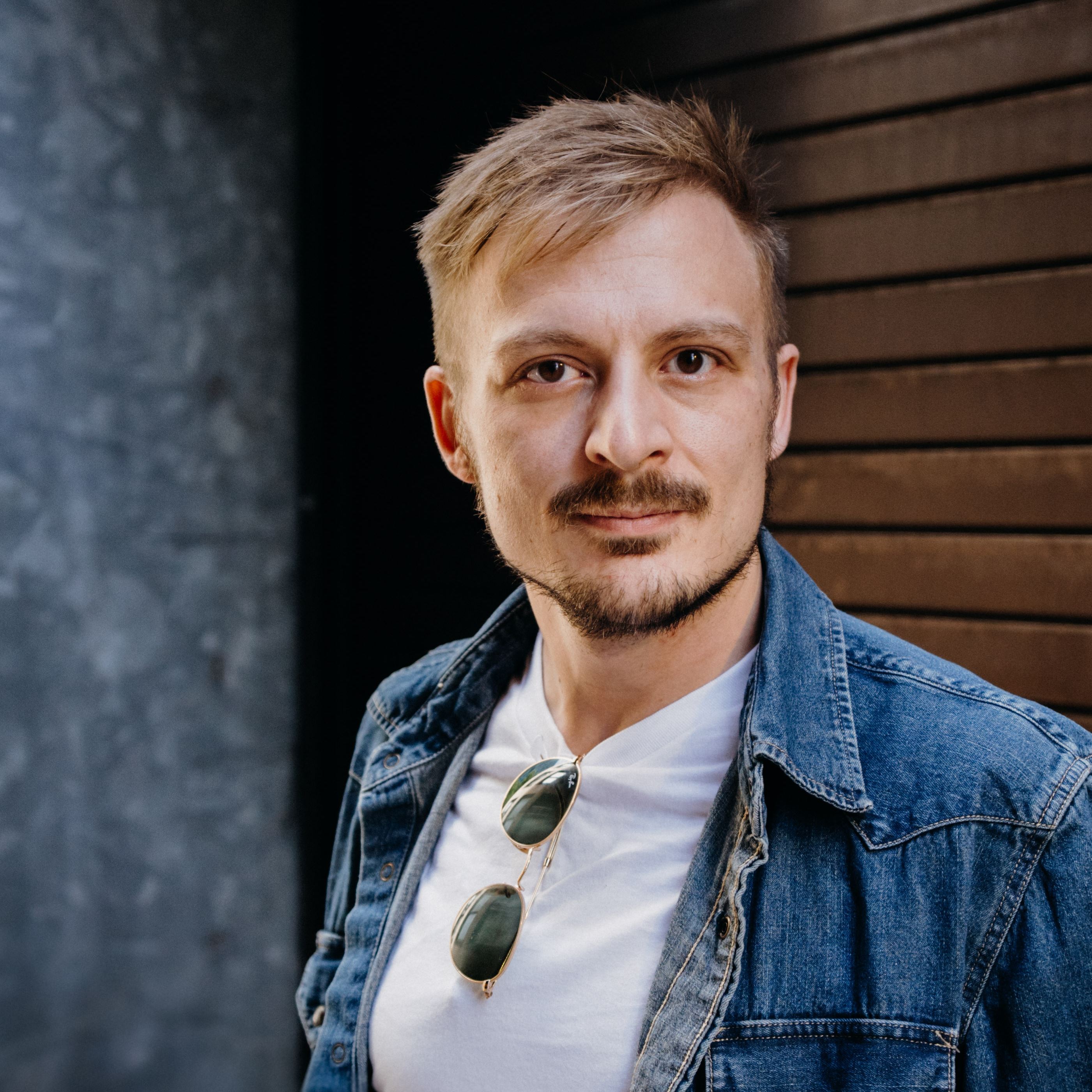 A close-up of Kyle Kiepert. He is wearing a white t-shirt with sunglasses and a denim jacket.