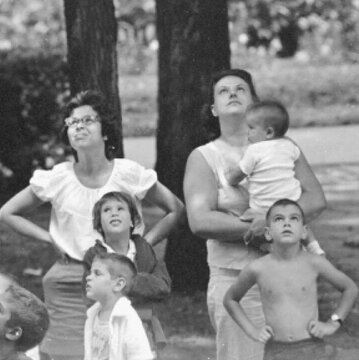 Black and white photo of a group of women and children looking upward and focusing on something above them.