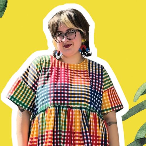 A person in a plaid and rainbow dress, rainbow earrings and glasses stands in front of a yellow background with green accents. 