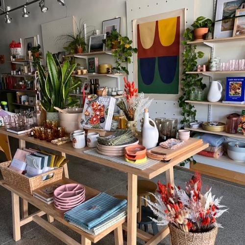 Tables and shelves in Good Day Shop are filled with products like vases, drinking glasses, pitchers, books and more. 