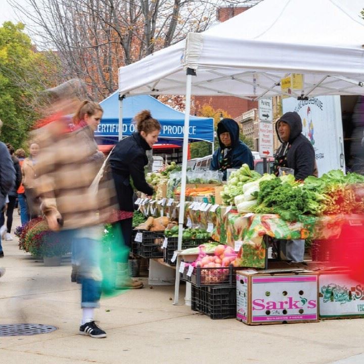 A booth at a farmers' market with people walking by.