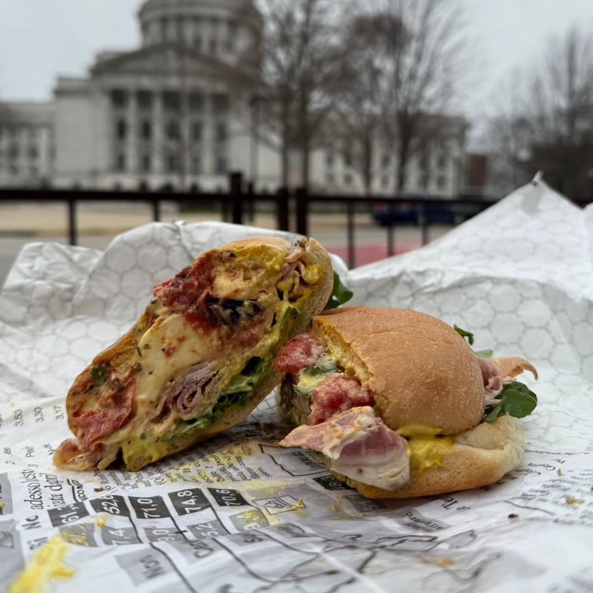On a piece of sandwich wrap, a cross-section of a sandwich is displayed. In the background is the Wisconsin Capitol building.