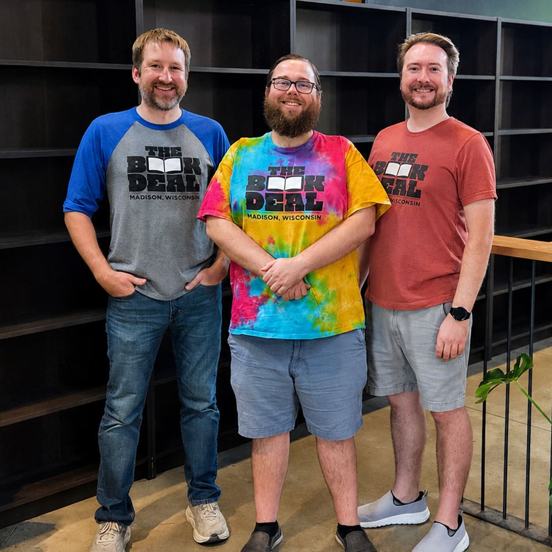 Three men with The Book Deal shirts stand in front of empty shelves.