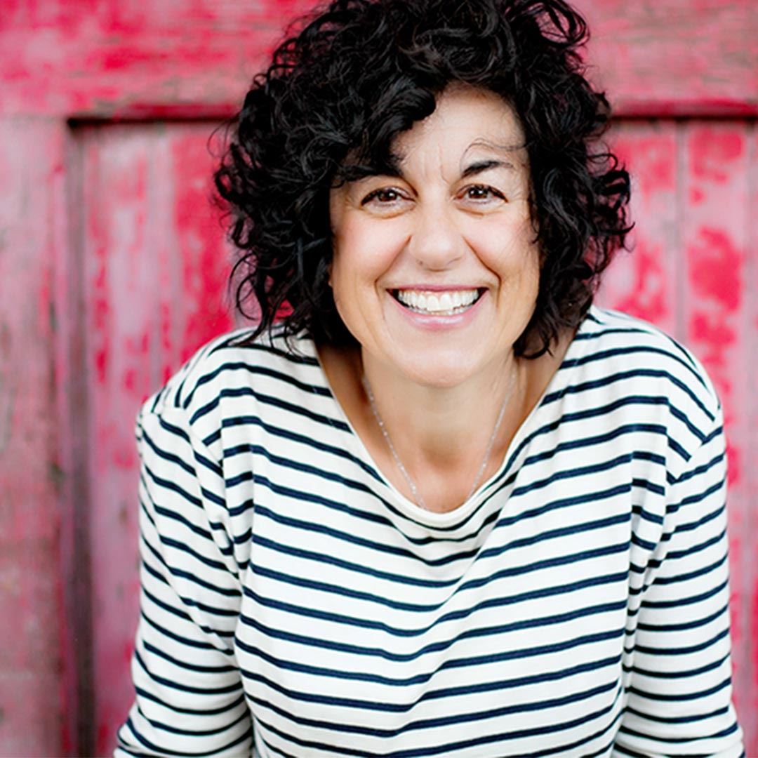 A headshot of a smiling woman with dark curly hair and a striped shirt.
